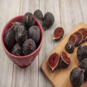 top view of delicious ripe black mission figs on a wooden kitchen board with black figs on a bowl on a grey wooden background